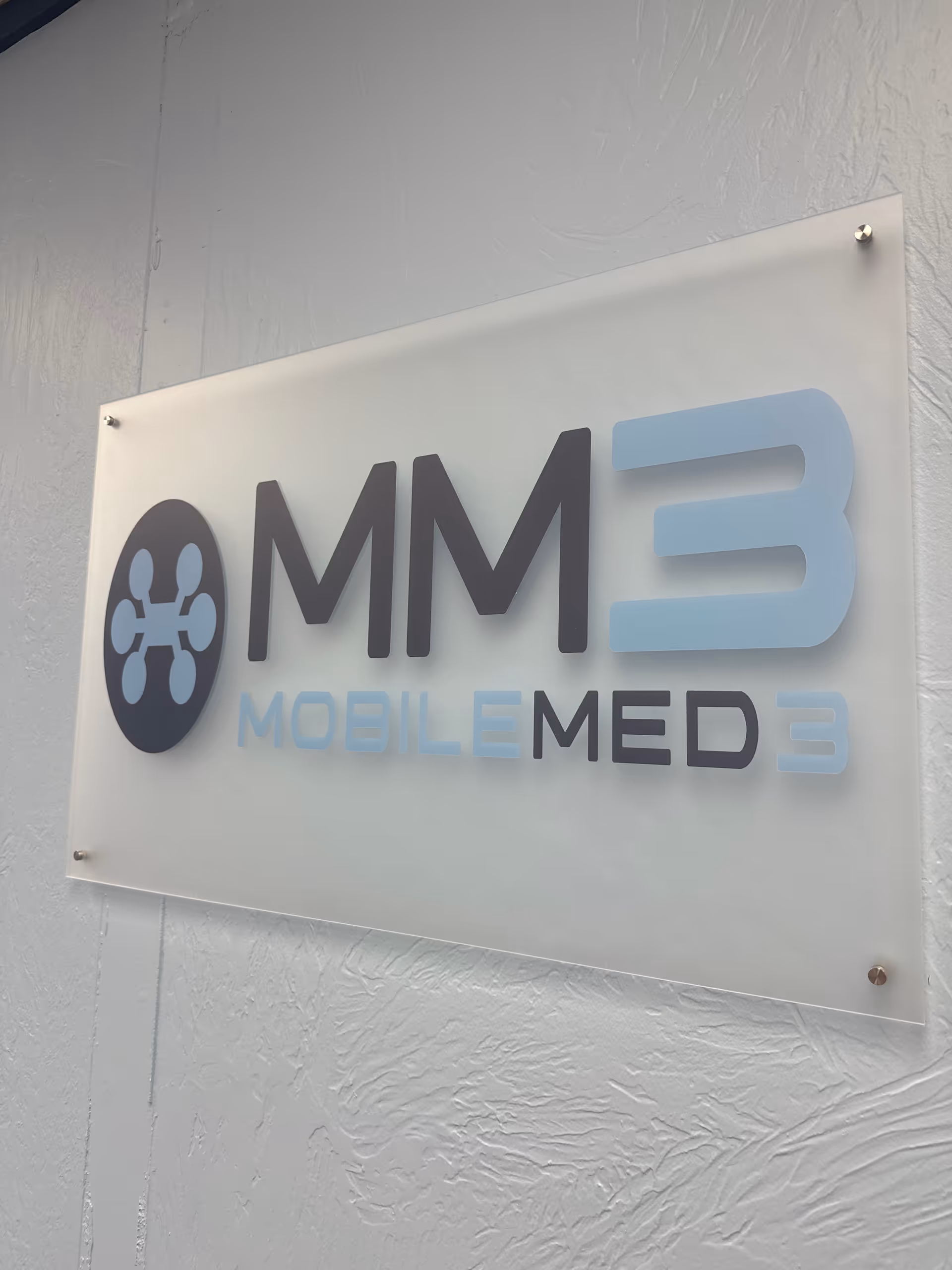 Exterior wall sign displaying MM3 Mobile Med logo on light-gray facade