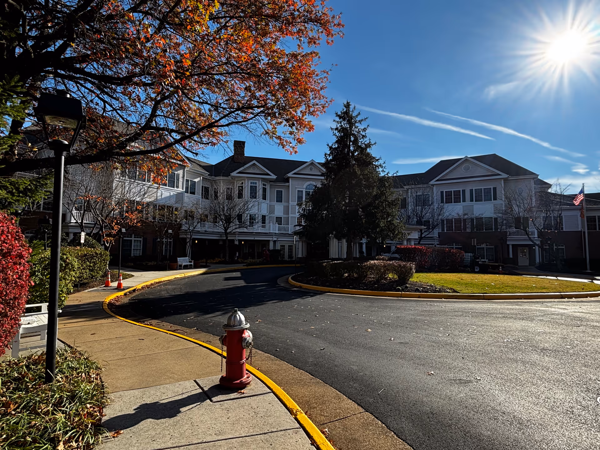 Circular driveway and landscaped front entrance of a multi-story senior living building under a bright sun.