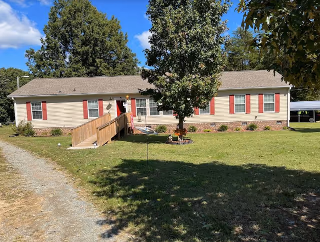 Front view of Evans Forever Young Family Care Home, ramp entrance, beige siding, red shutters, lawn.