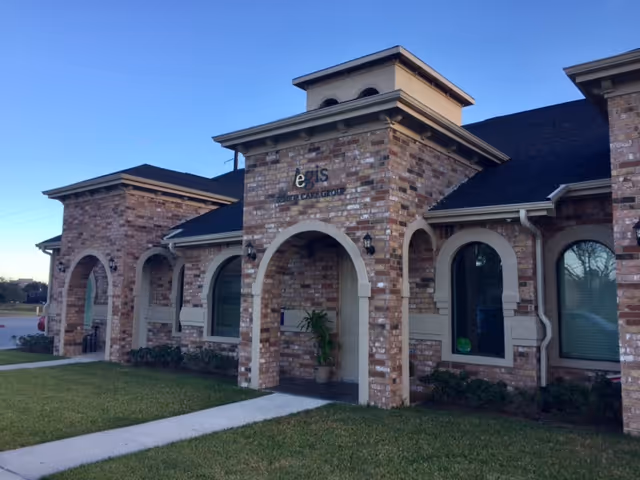 Exterior view of a brick senior care facility with arched entryways and a manicured lawn.