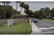 Exterior view of Arrowwood Lane facility with entrance road, sign, and palm trees.
