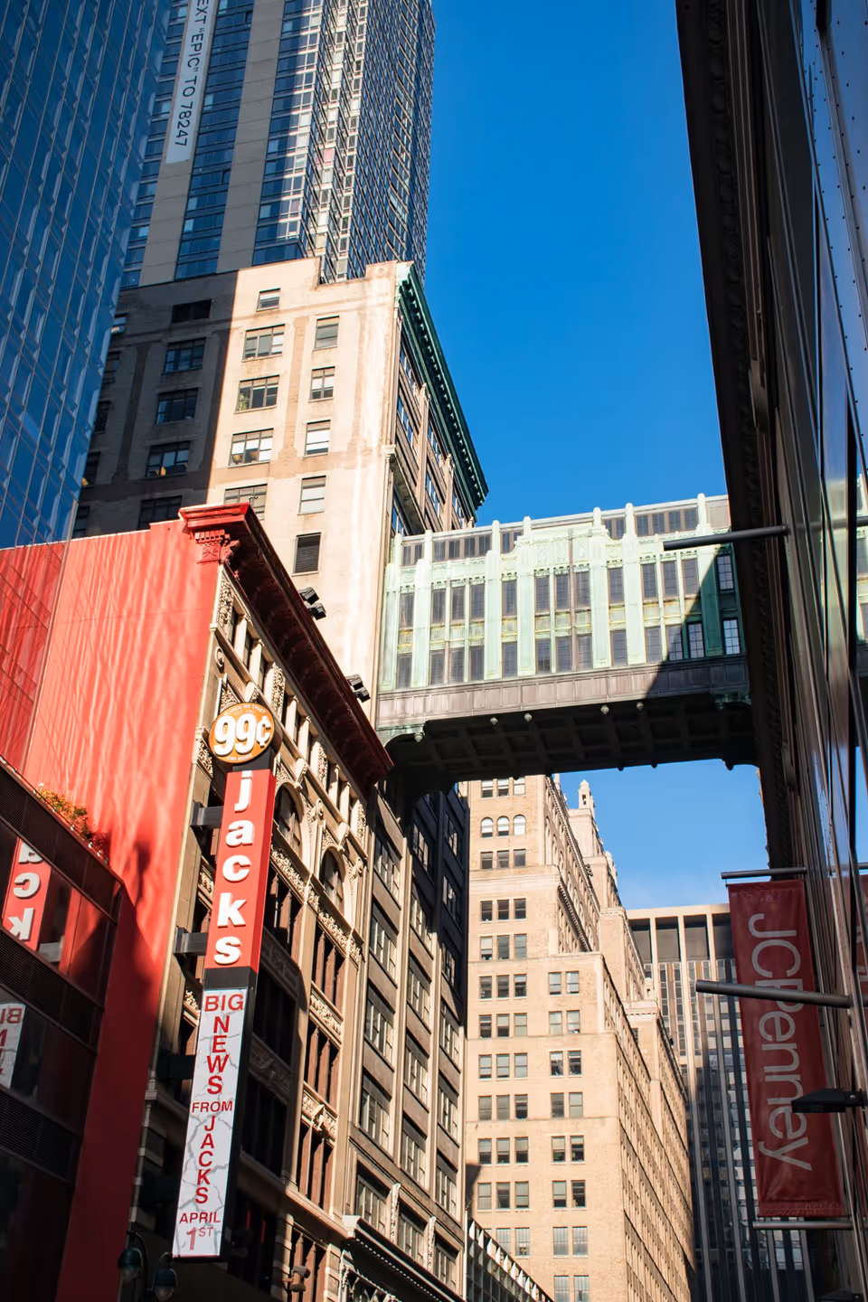 Tall city buildings with a pedestrian skybridge against a bright blue sky