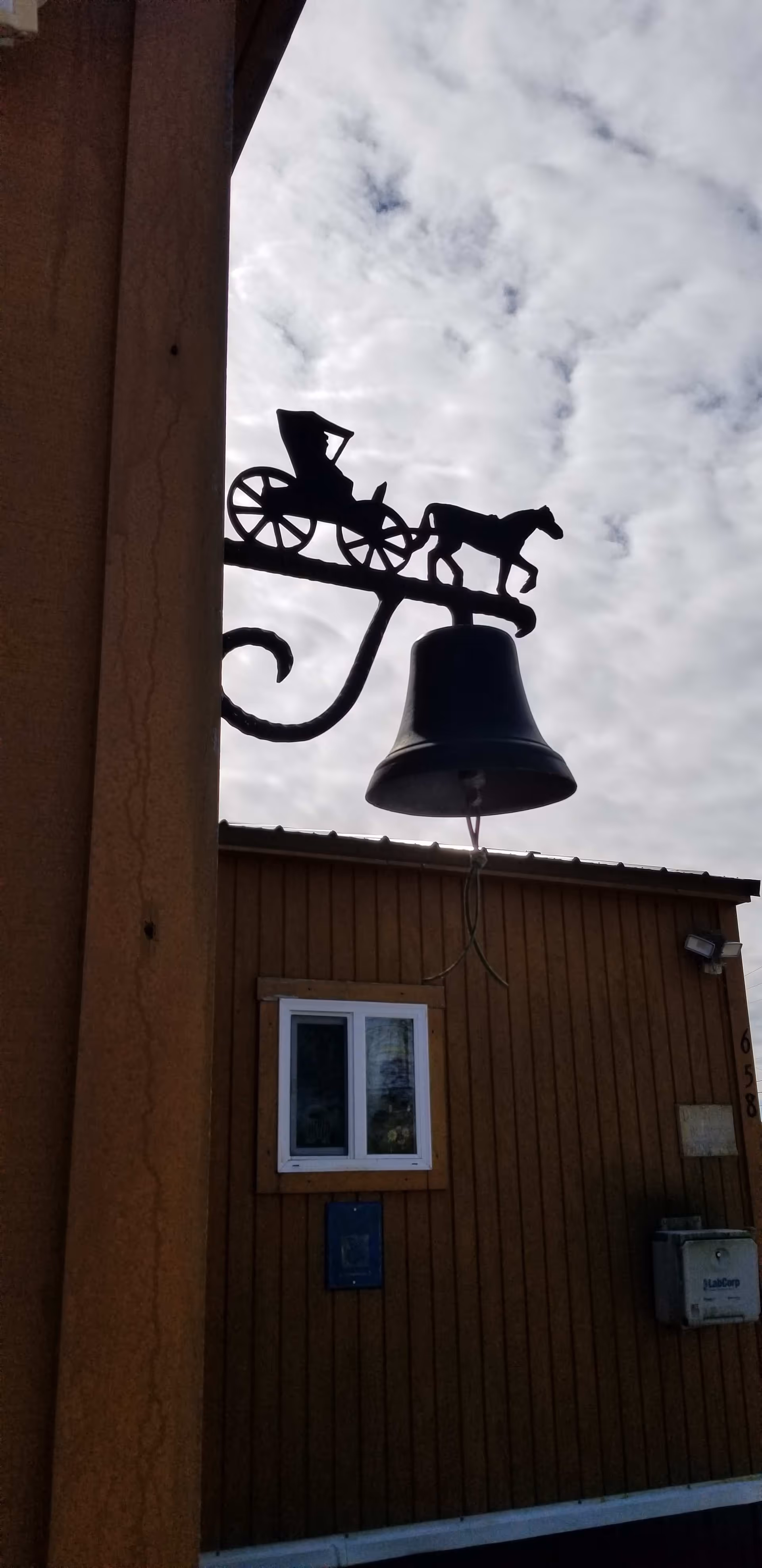 Exterior view of brown wooden building with a horse-drawn carriage bell silhouette against cloudy sky