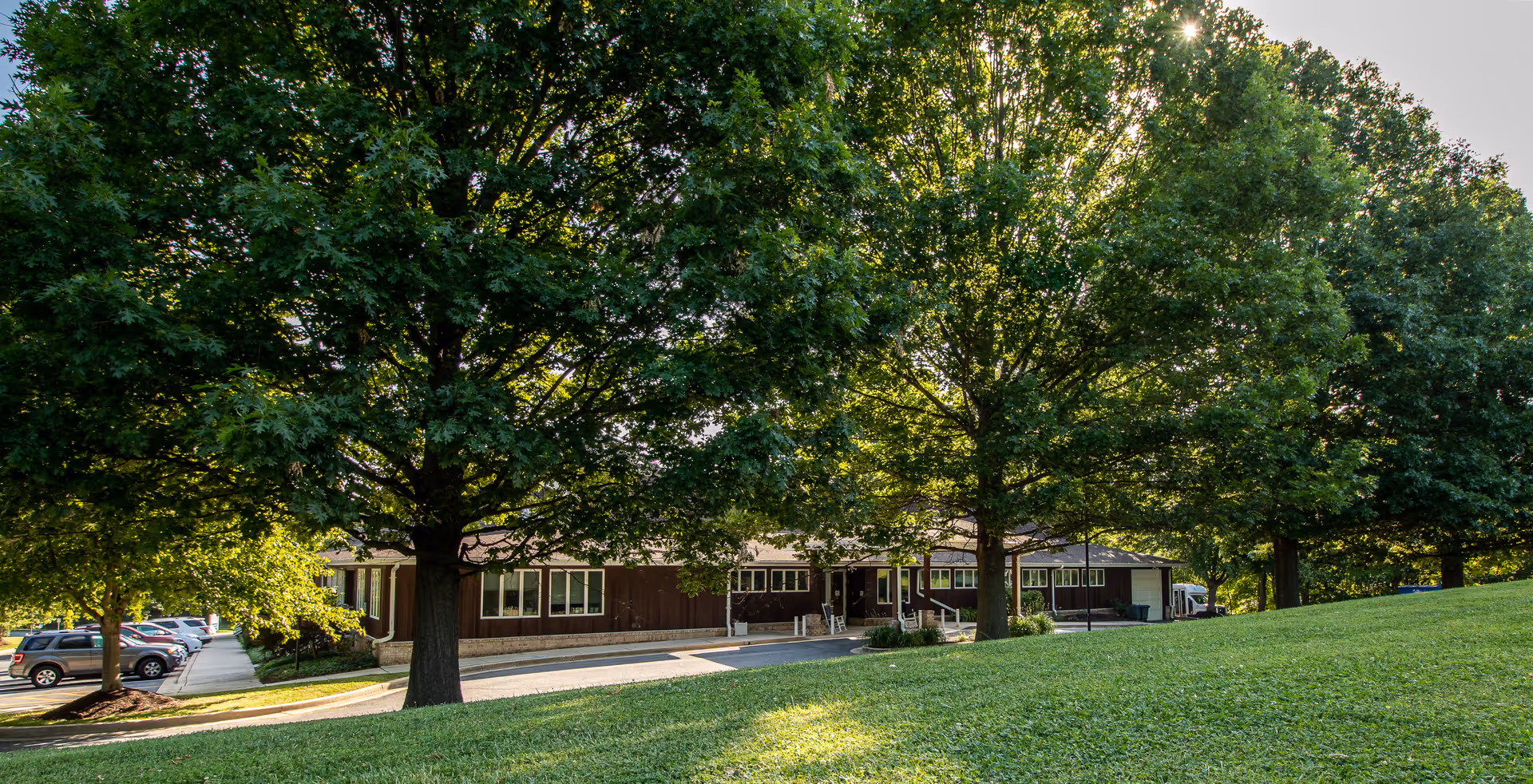 Front exterior of Winter Growth Marge's Memory Care, shaded by trees beside a parking lot.