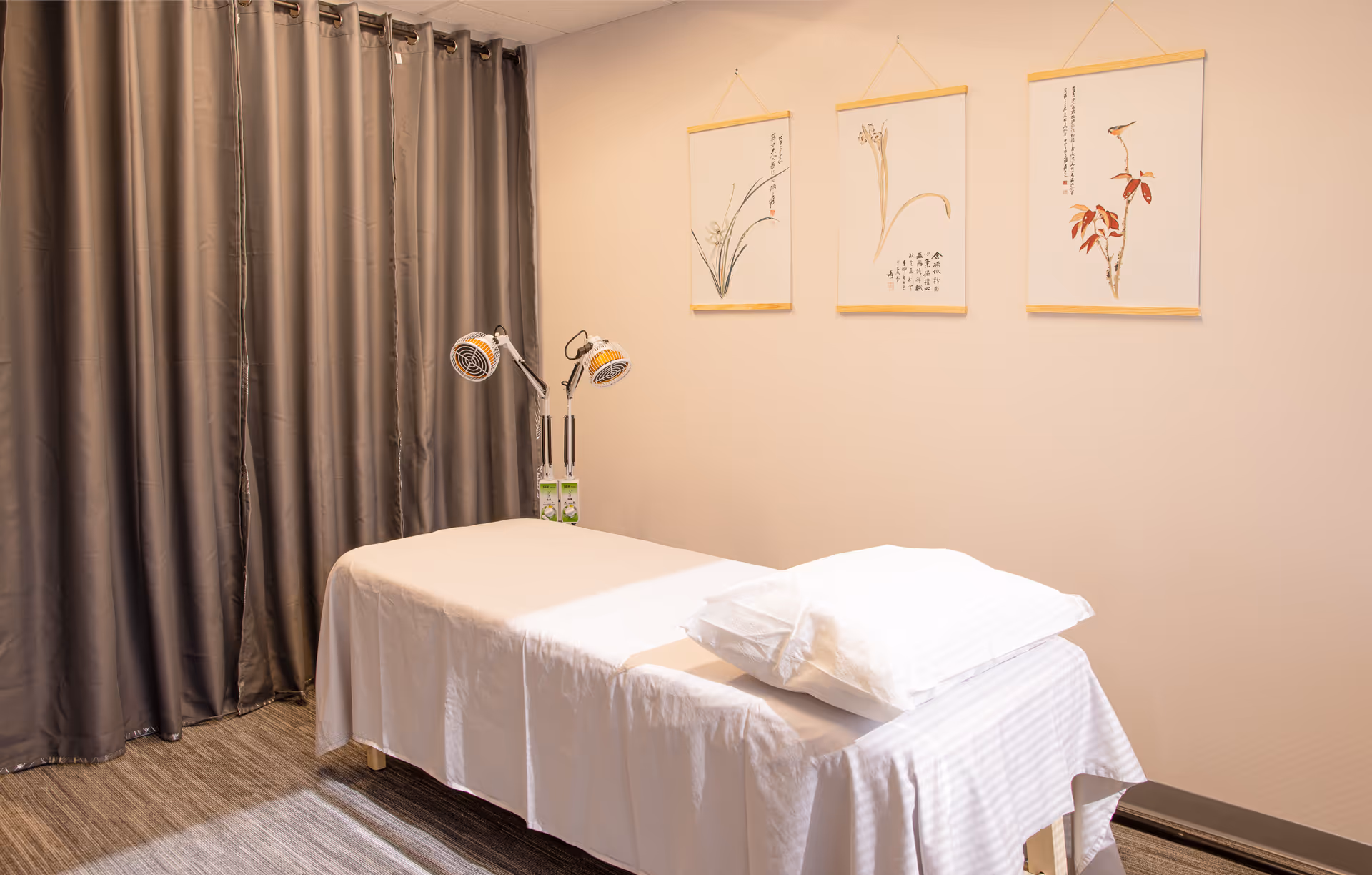 Treatment room with a white therapy table, pillows, lamps, curtains, and wall art.