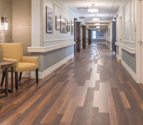 Well-lit interior hallway with patterned wood flooring, seating, and framed artwork along the walls.