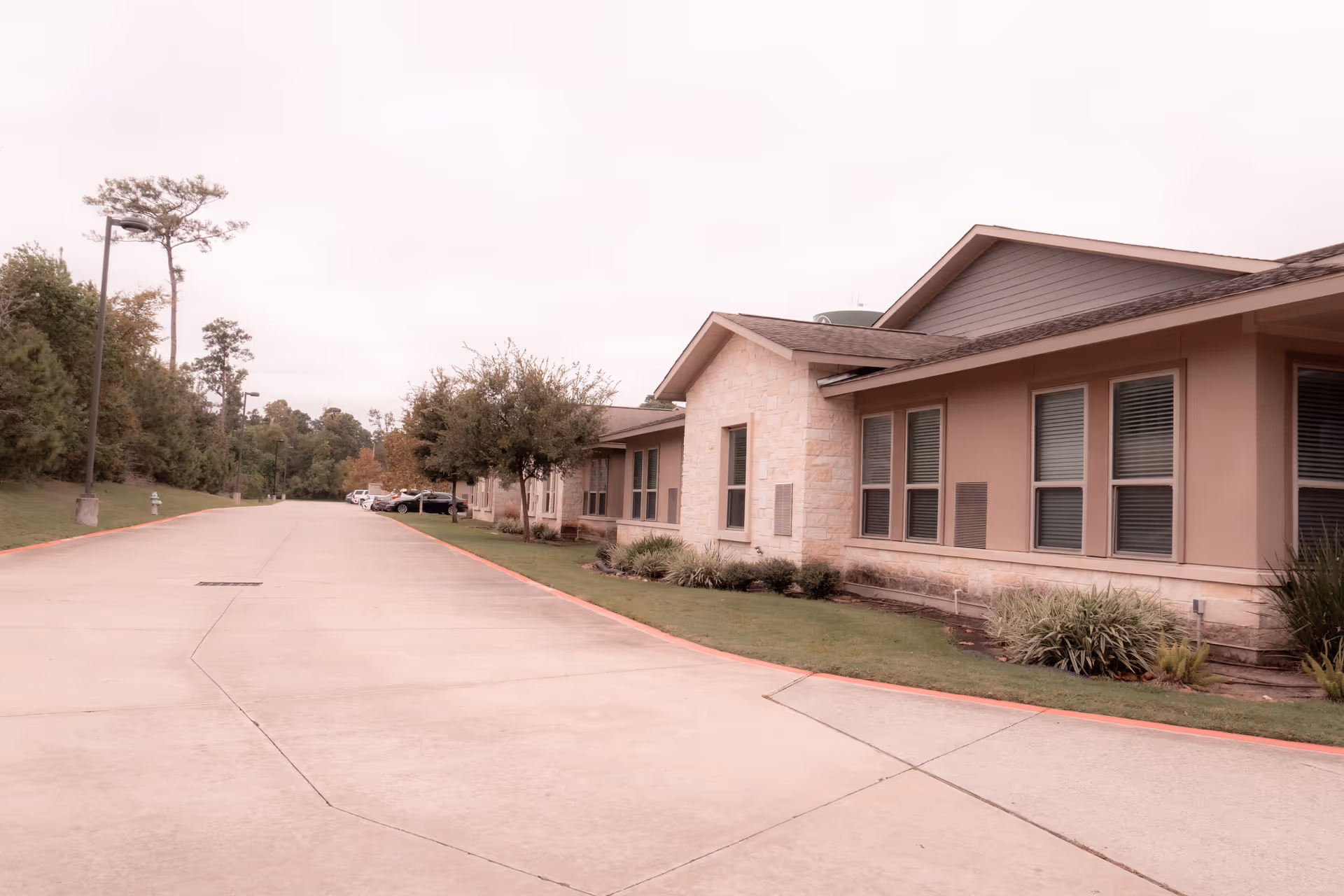 Driveway leading past a single-story senior living facility building with landscaped lawn and windows.