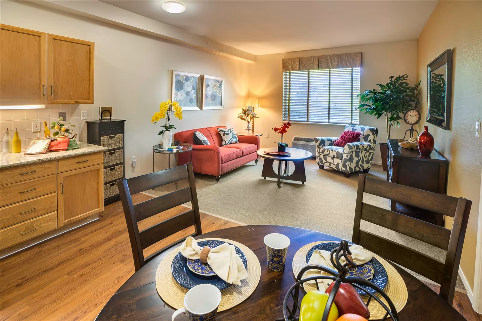 Open-concept living area with kitchen, dining table, red sofa, and patterned chair.