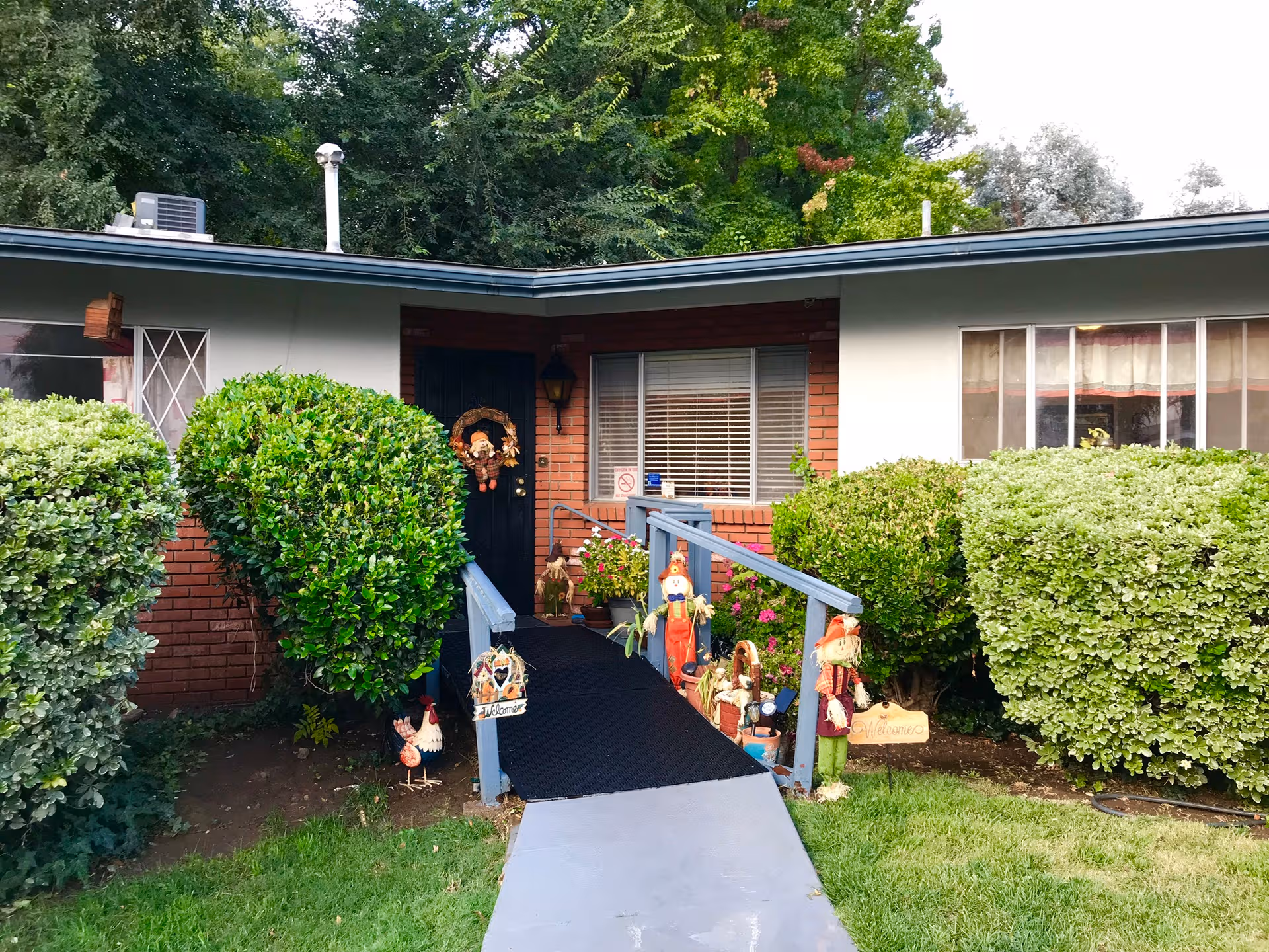 Front entrance of a single-story senior home with a ramp and trimmed hedges.