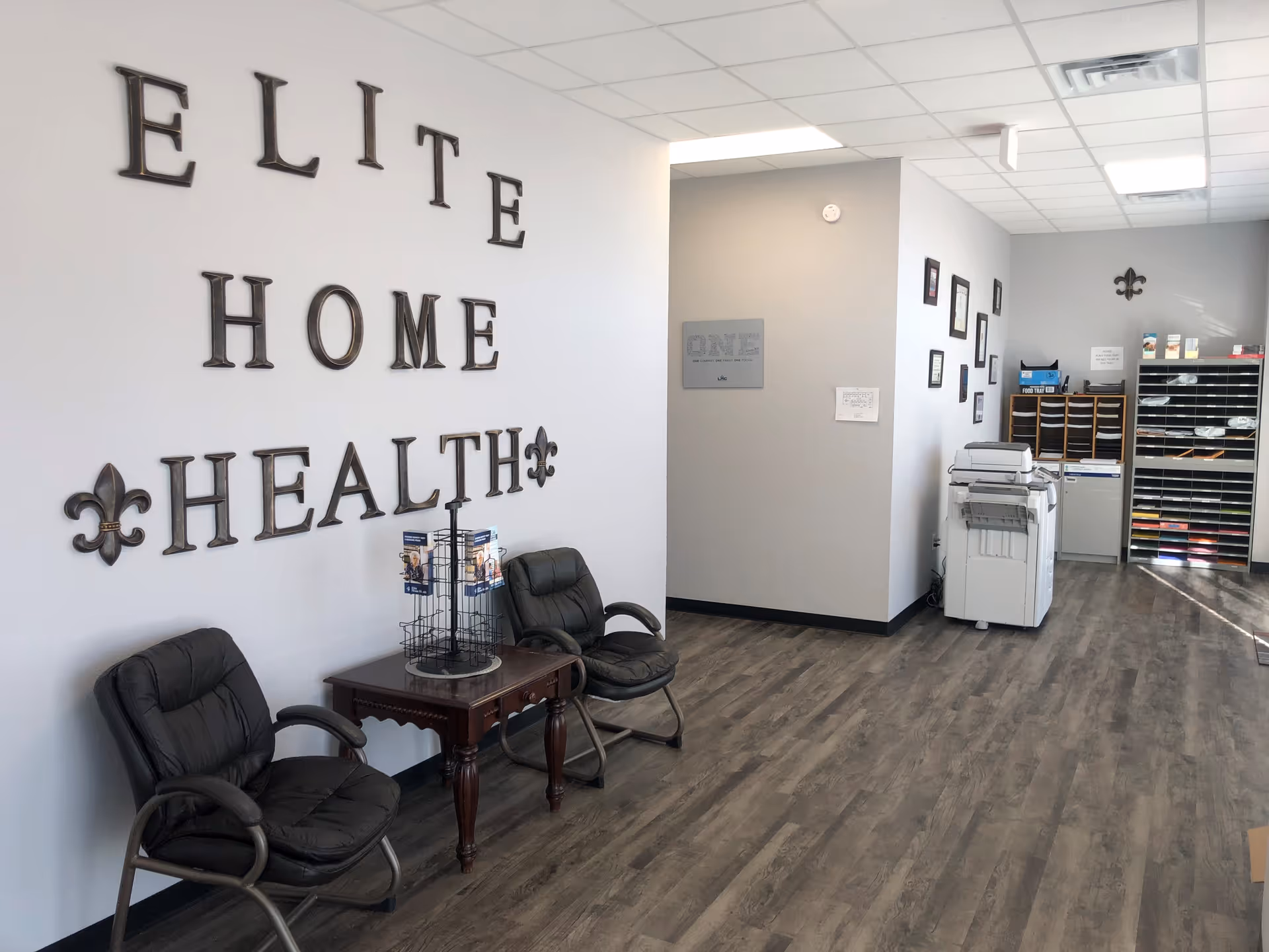 Interior lobby of Elite Home Health with chairs, table, copier, and shelves.