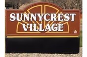 A large wooden Sunnycrest Village sign outdoors with trees behind.