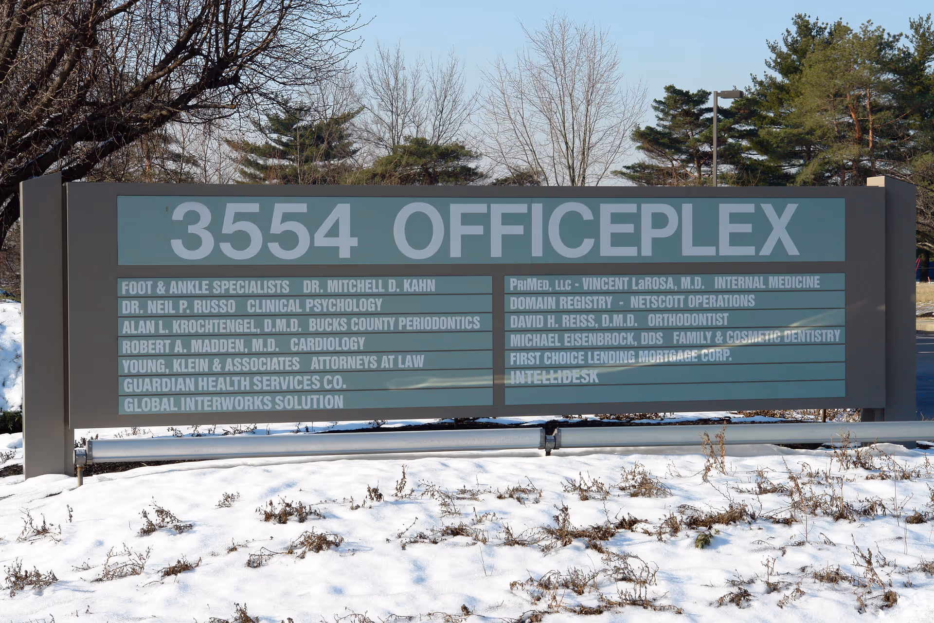 Large gray OFFICEPLEX sign listing tenants sits in a snowy landscape.