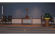 Chapel-style sanctuary interior with altar, cross, candles, chairs, and a lectern.