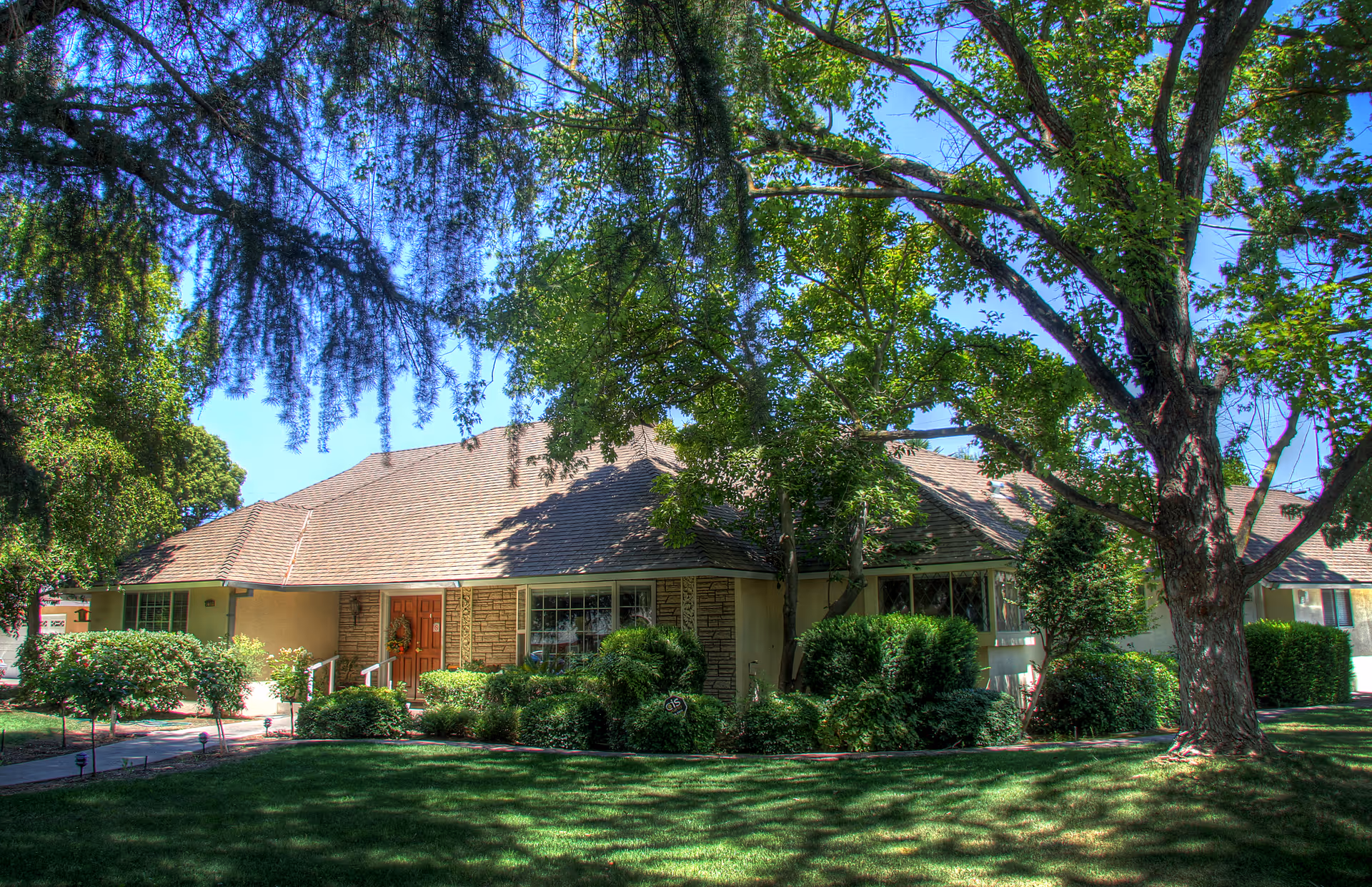 Single-story senior living facility entrance with well-kept lawns and large trees in front.