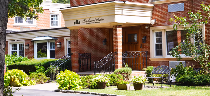 Brick building entrance for Birchwood Suites with landscaped garden and bench.