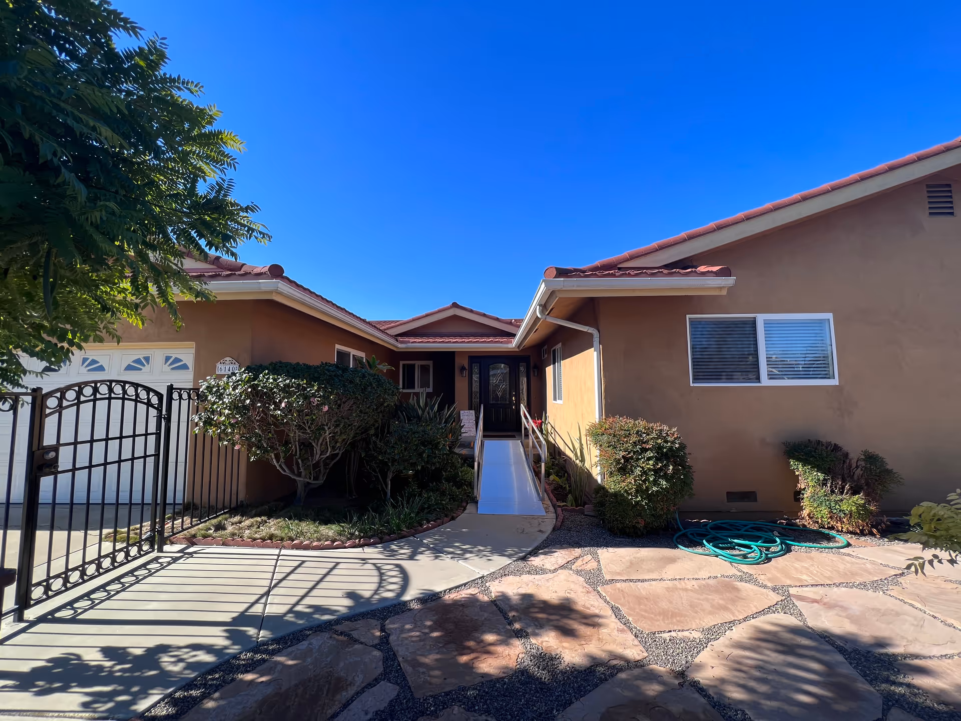 A single-story tan senior living facility with a central entrance, a gate, and landscaped front yard.