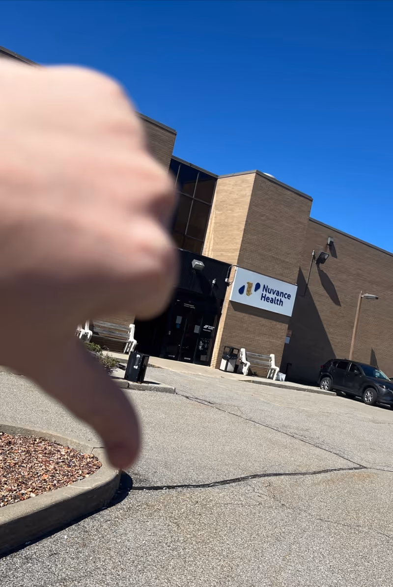 Foreground thumb obscures the exterior view of Nuvance Health Medical building.