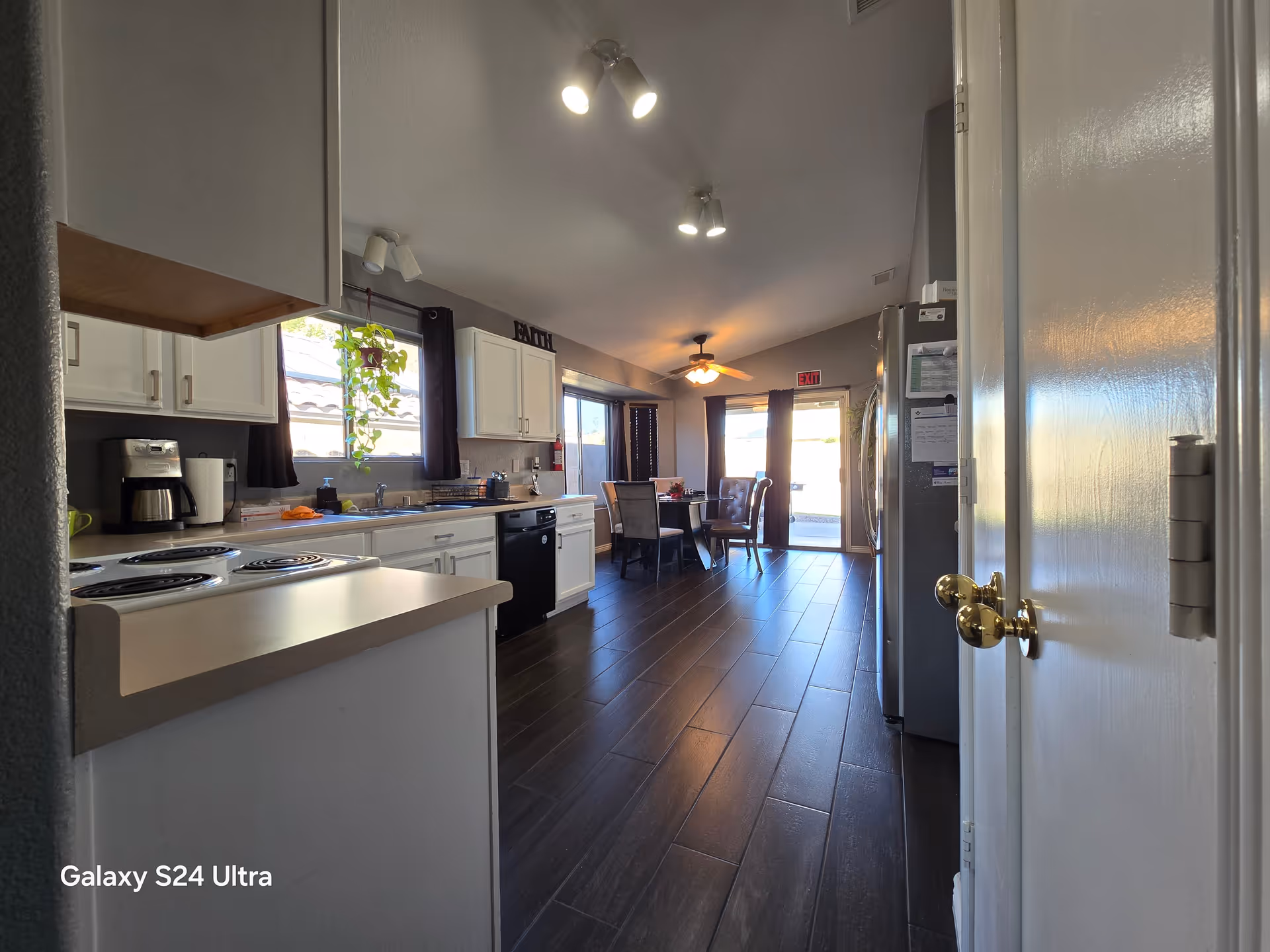 A long kitchen with white cabinets, dark floors, and a dining area at the far end.