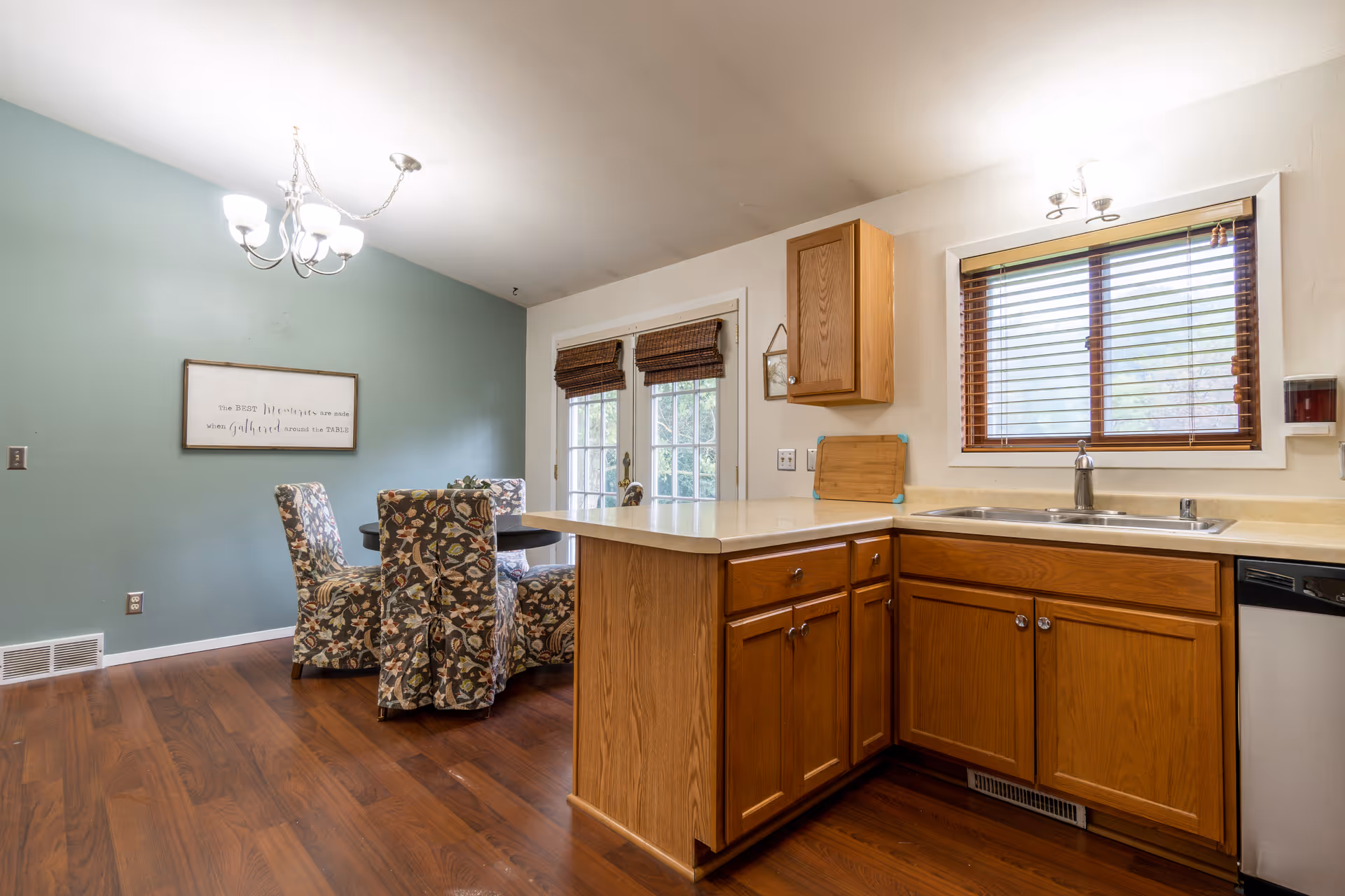 Open-concept kitchen with wooden cabinets, a sink, and a dining area against a teal wall.