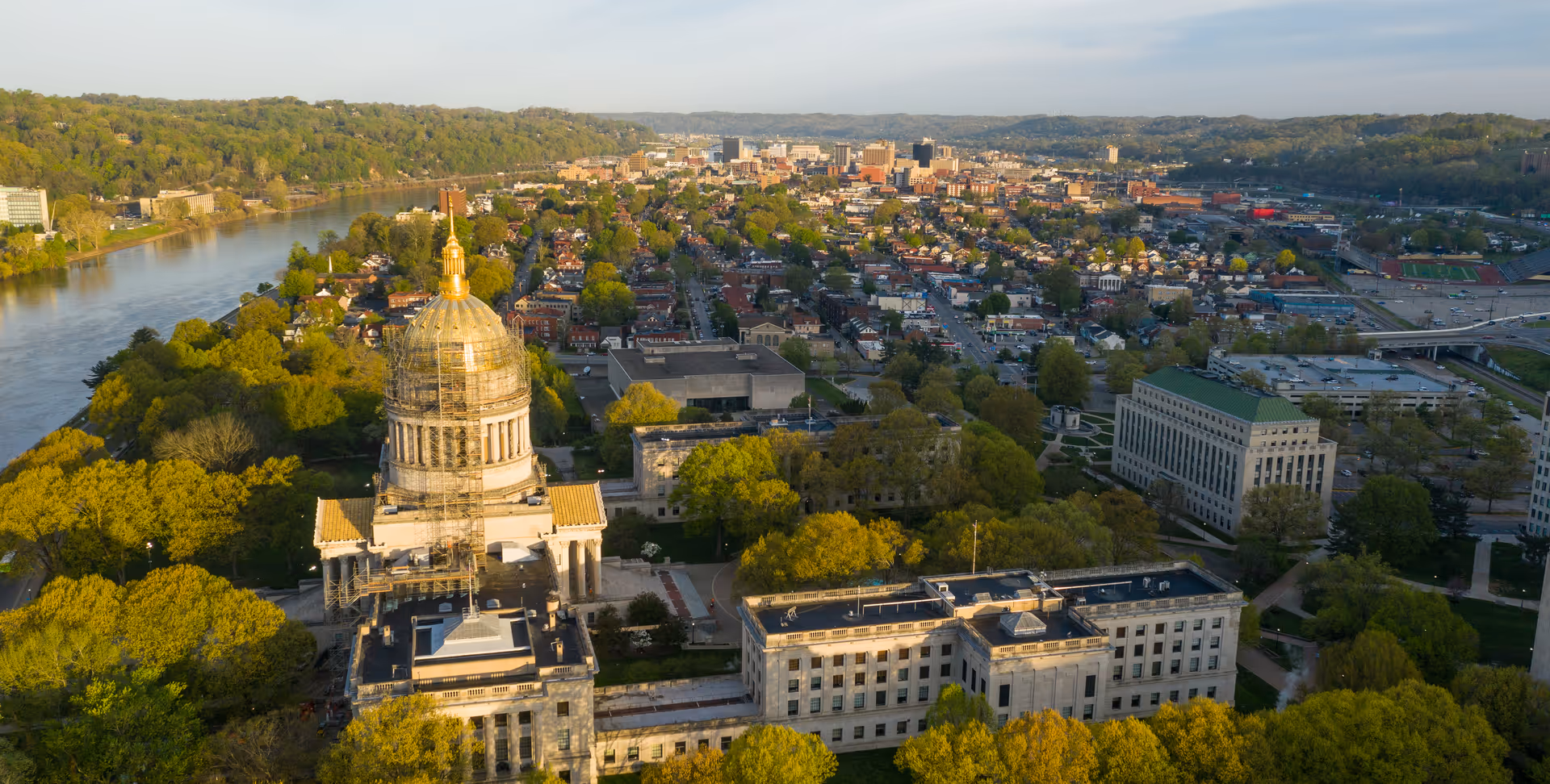 Aerial view of a city and river with a domed capitol building surrounded by trees.