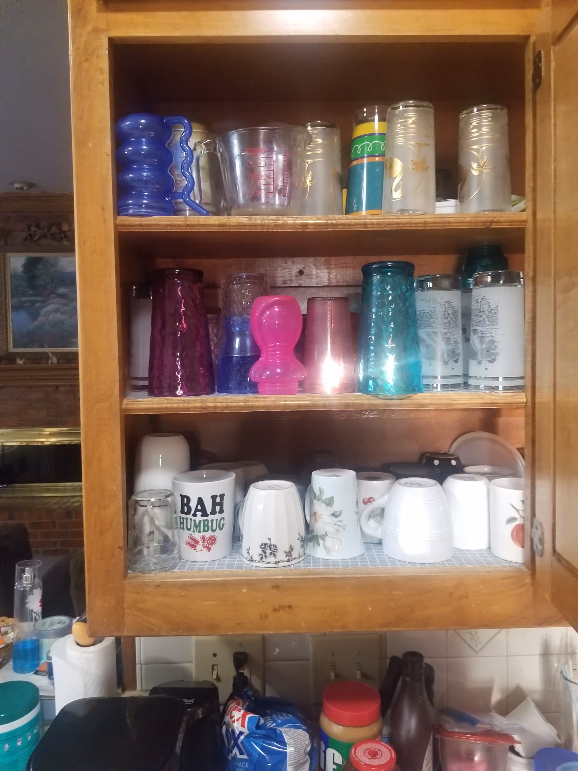 Open kitchen cabinet filled with mugs, cups, and glassware on wooden shelves.