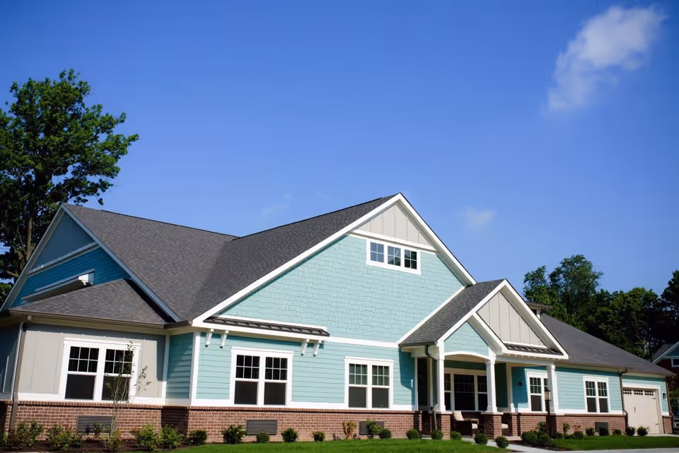 Front exterior of a light blue, single-story residential building with gabled roofs, white trim, and a manicured lawn.