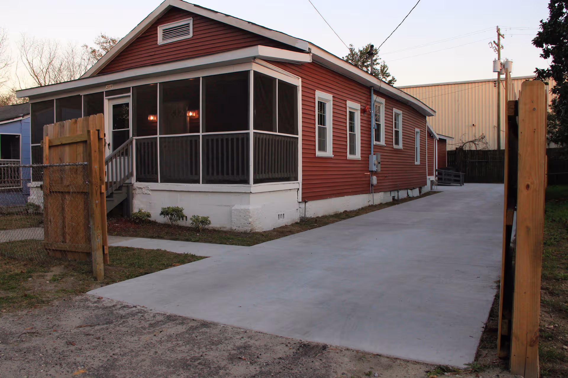 Red single-story care home with screened porch, concrete driveway, and wooden gate.