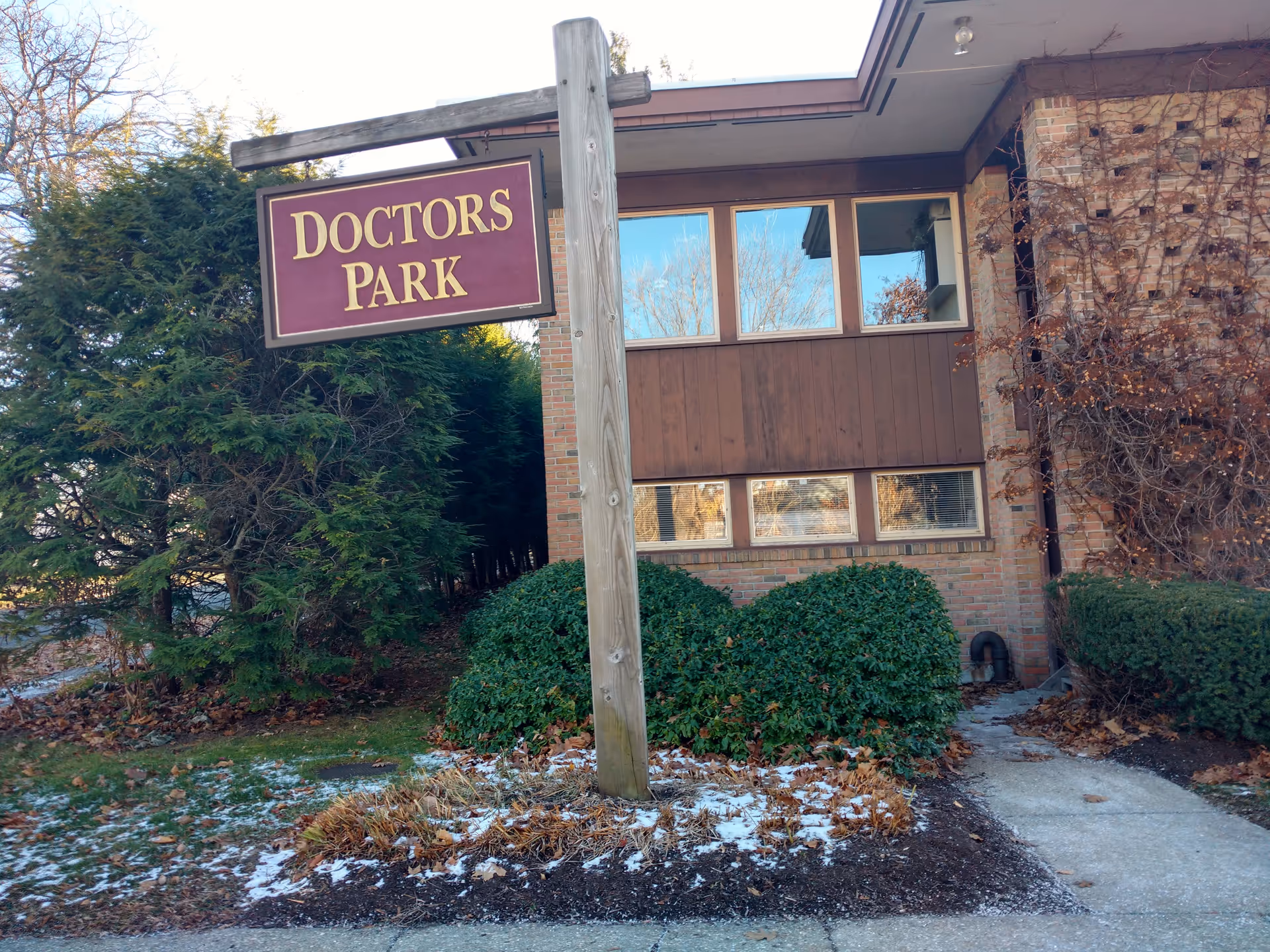 Exterior view of a brick building with a tall wooden Doctors Park sign.