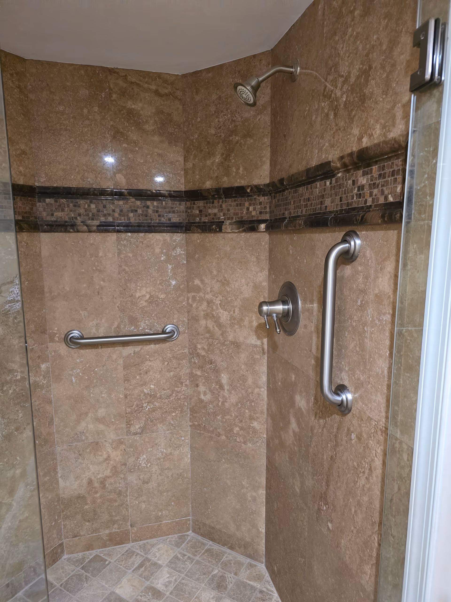 Accessible shower with beige tiles, grab bars, and a handheld showerhead.