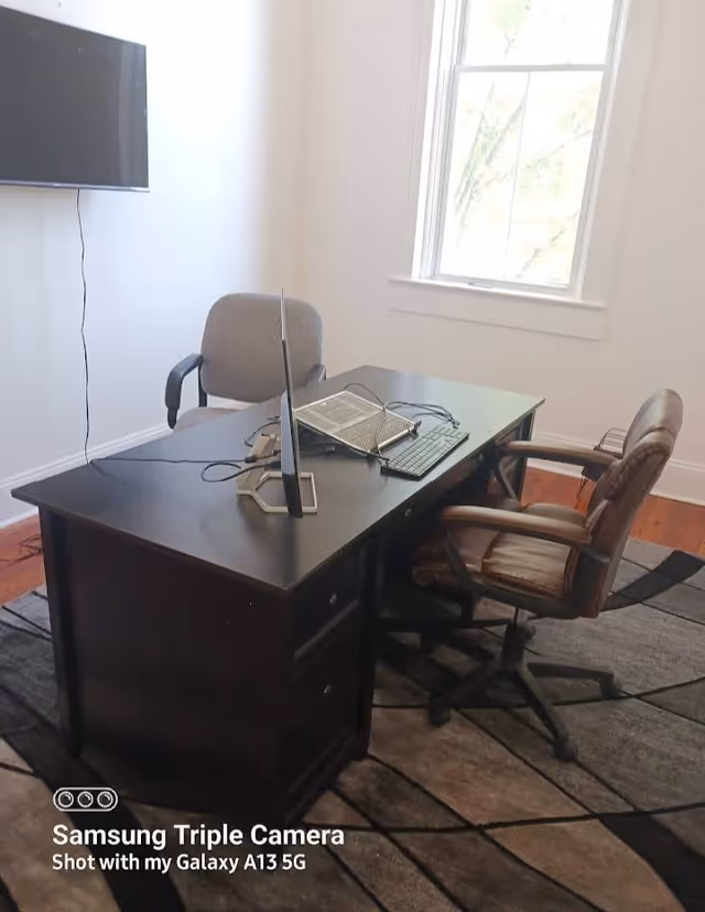 Compact home office setup with desk, computer, laptop, and a window in a bright room.