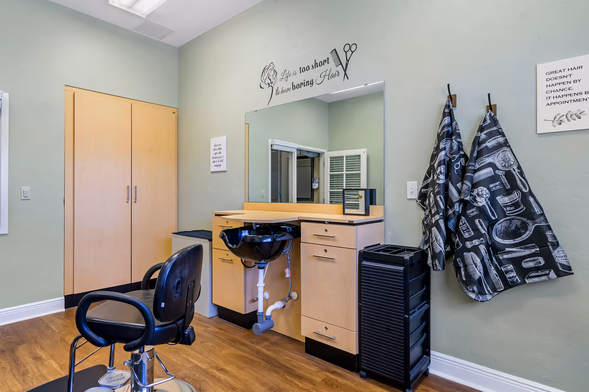 Hair salon station with chair, sink, mirror, and cabinets in care facility.