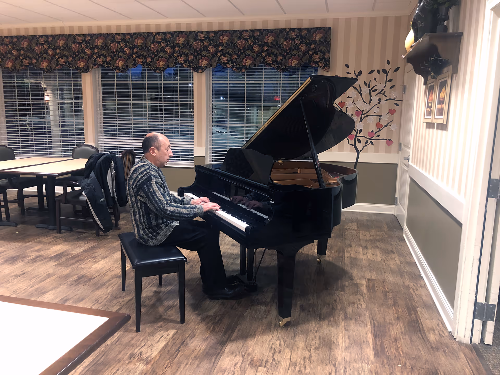 A man plays a grand piano in a well-lit community room.