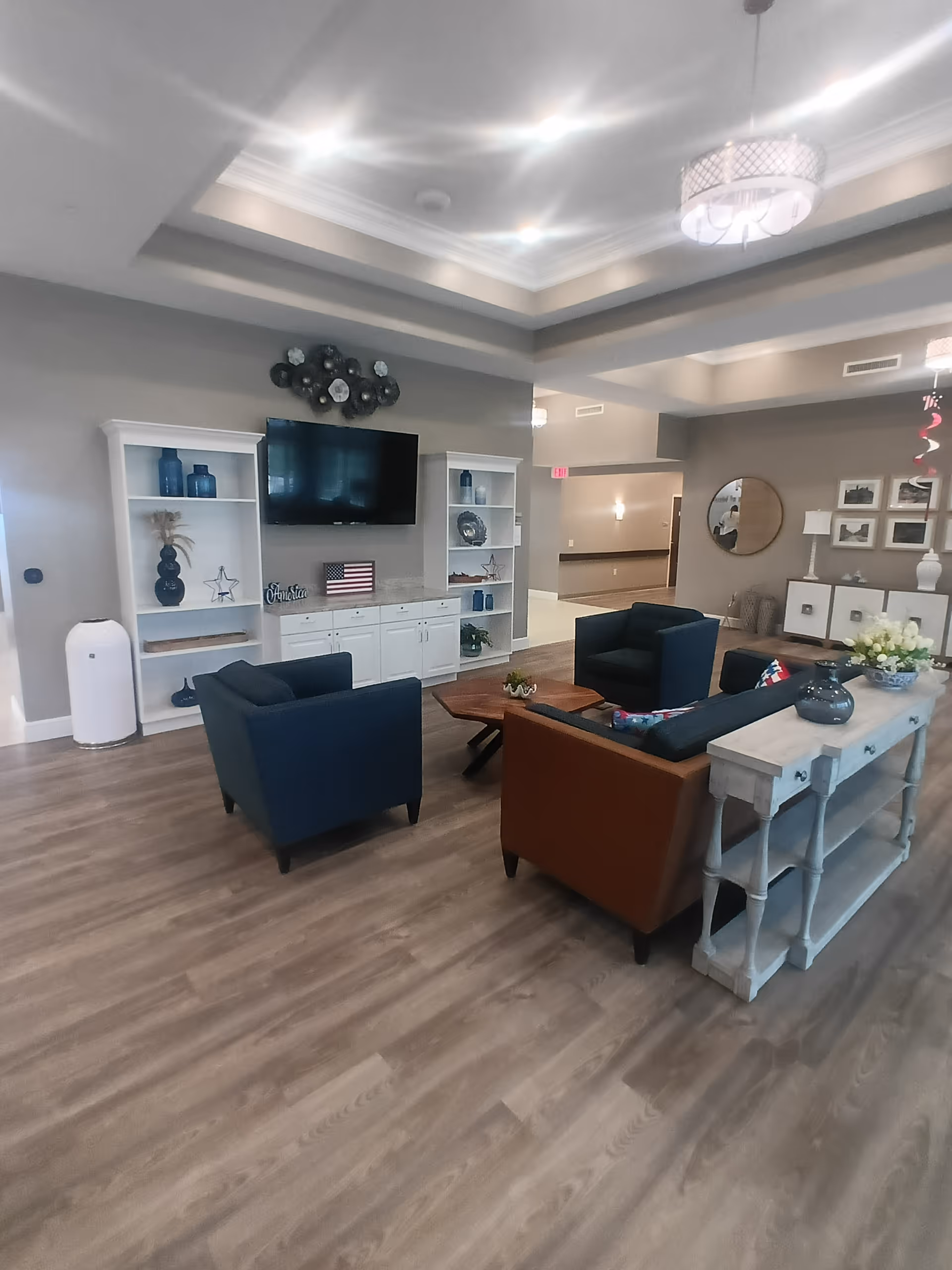 Spacious senior living lounge with blue chairs, sofa, TV, and decorative shelving.
