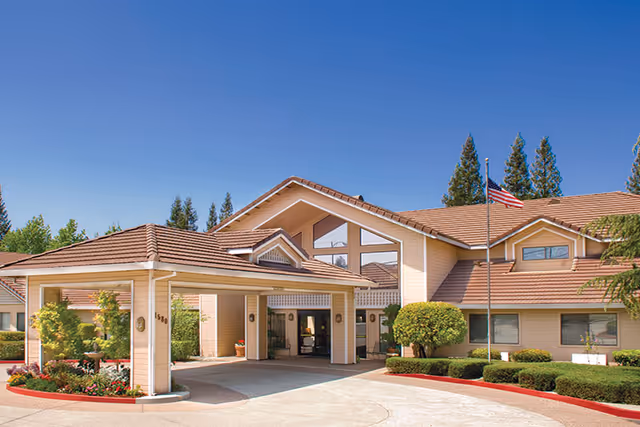 Front exterior of The Kensington at Walnut Creek, entrance canopy with flag and landscaped surroundings.