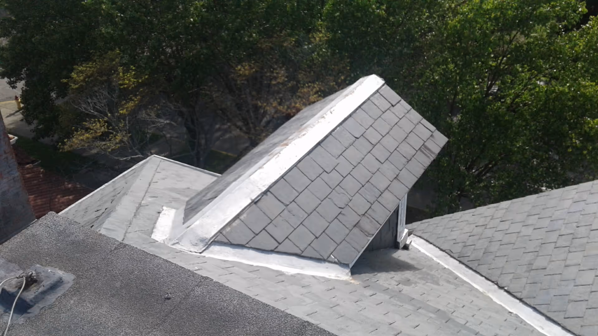 Exterior view of gray shingled rooftops with green trees in the background.