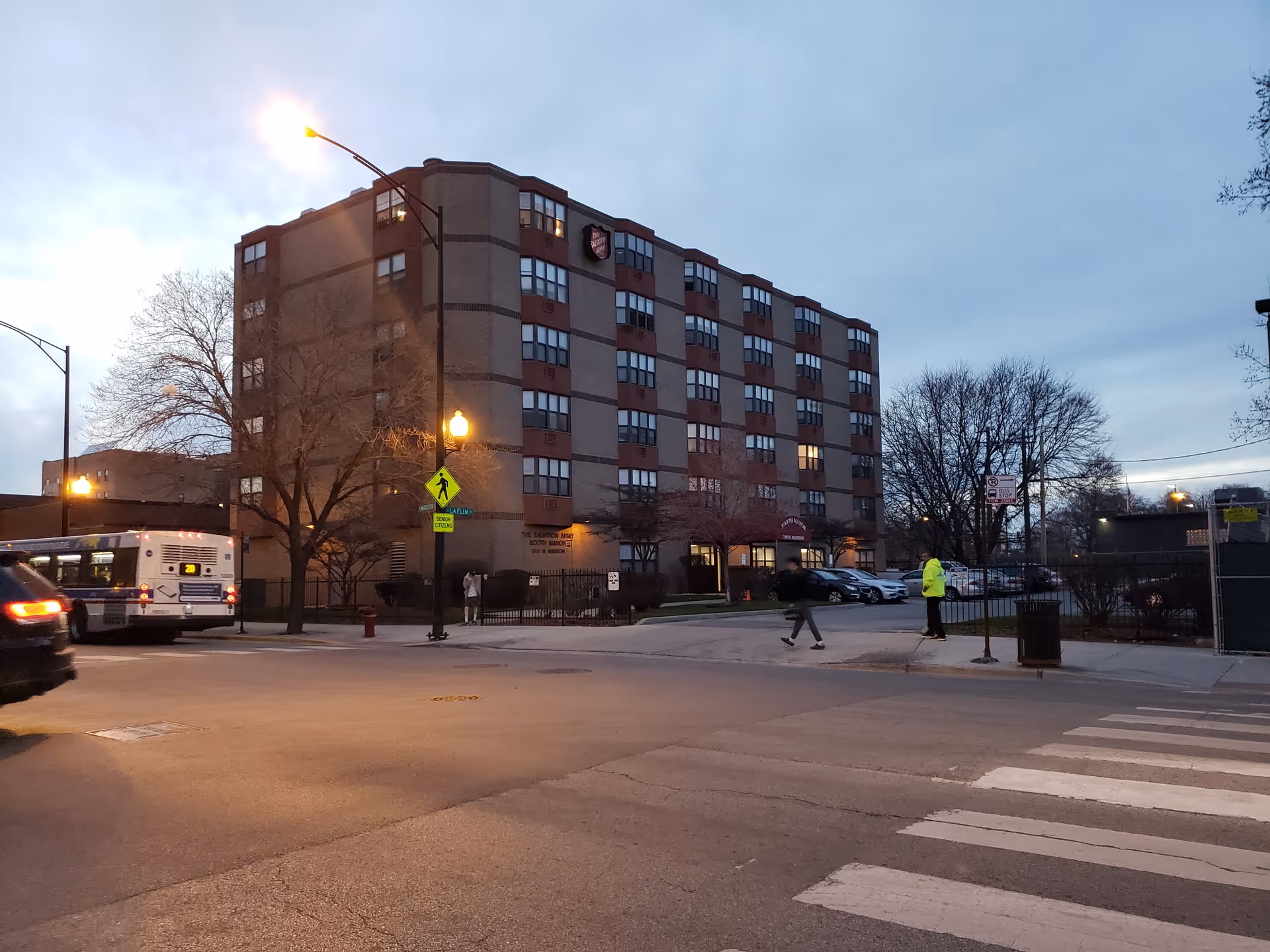 Multi-story brick senior residence seen from street with crosswalk and bus.
