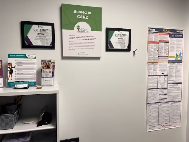 Interior wall with framed certificates and a central 'Rooted in CARE' sign above brochures.