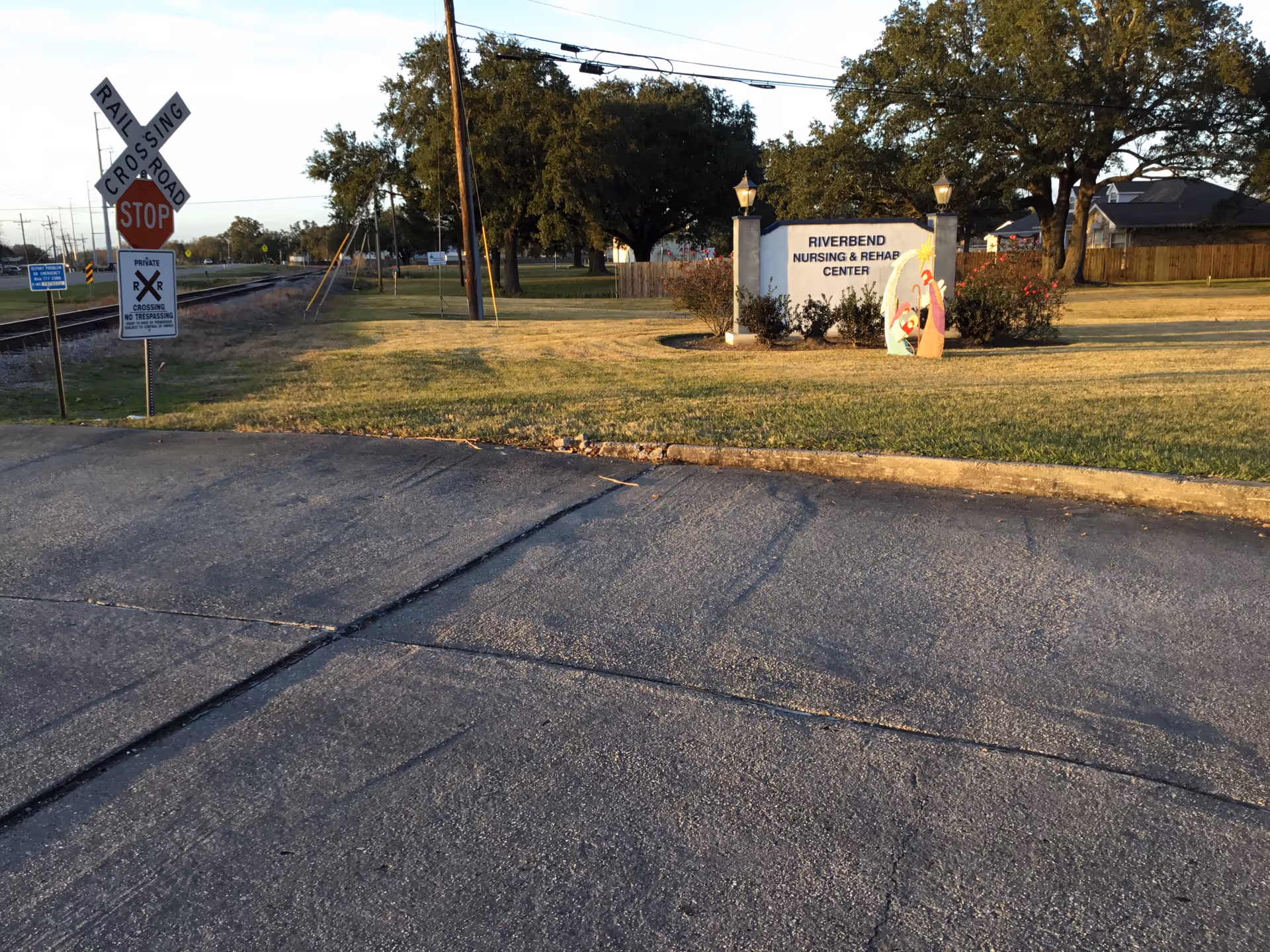 Outdoor view of street with Riverbend Nursing and Rehab Center sign and railroad crossing nearby.
