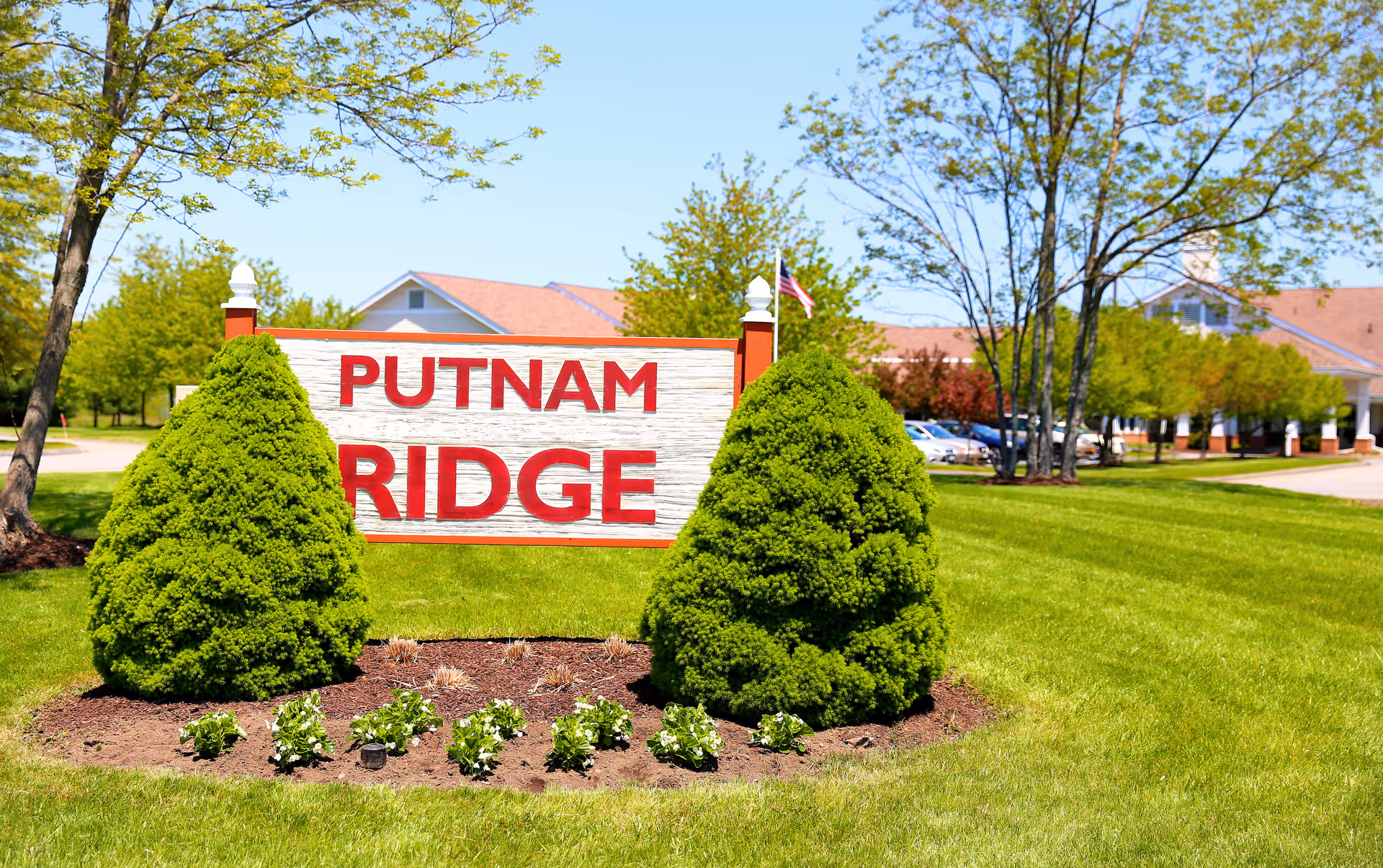 Front lawn with Putnam Ridge sign, trees, and a building in background.