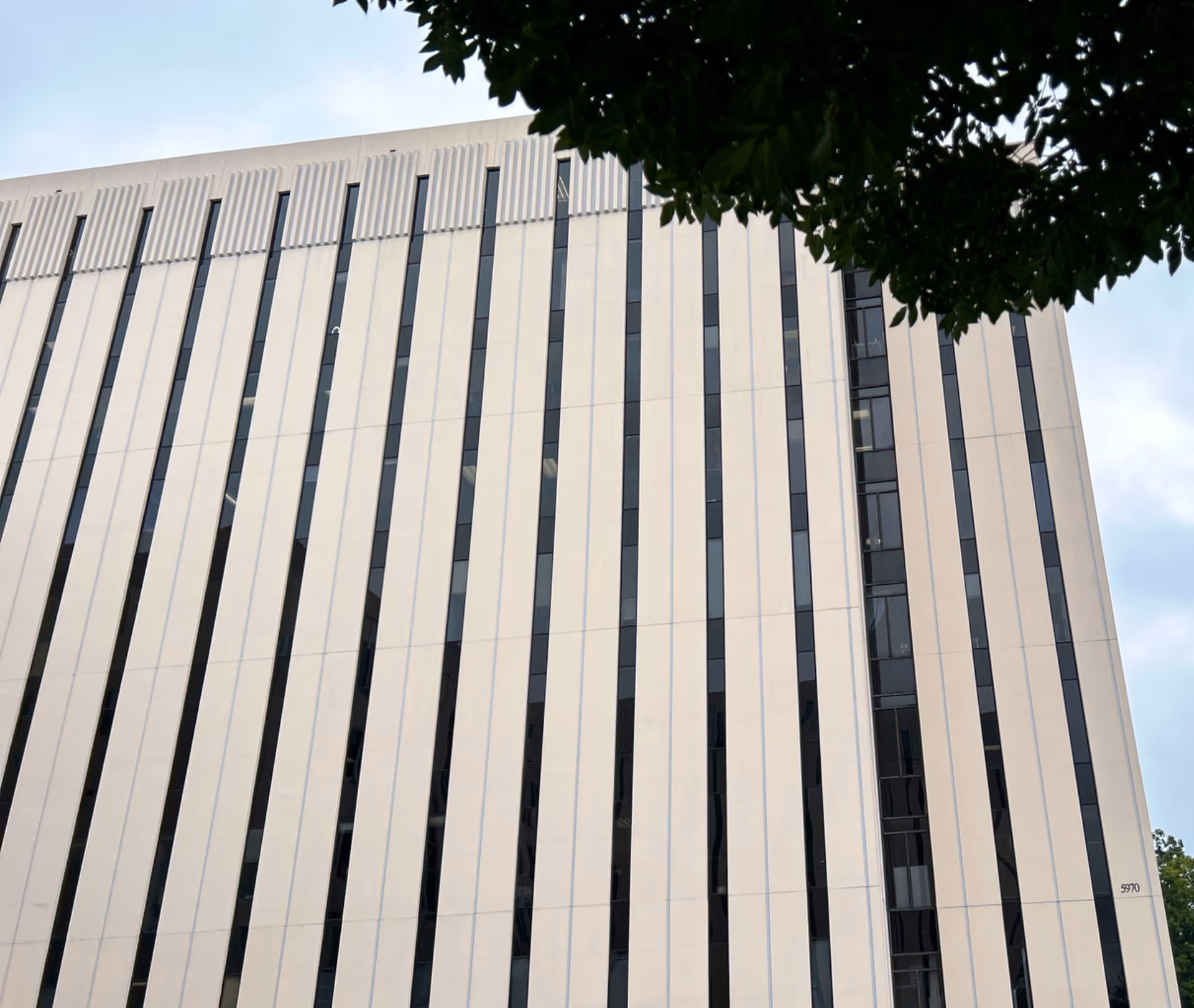 Exterior view of a modern multi-story facility with vertical beige panels and narrow windows.