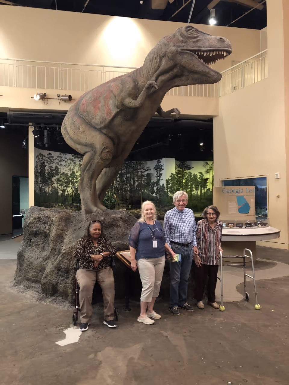 Group of four visitors beside a large dinosaur statue in a museum.