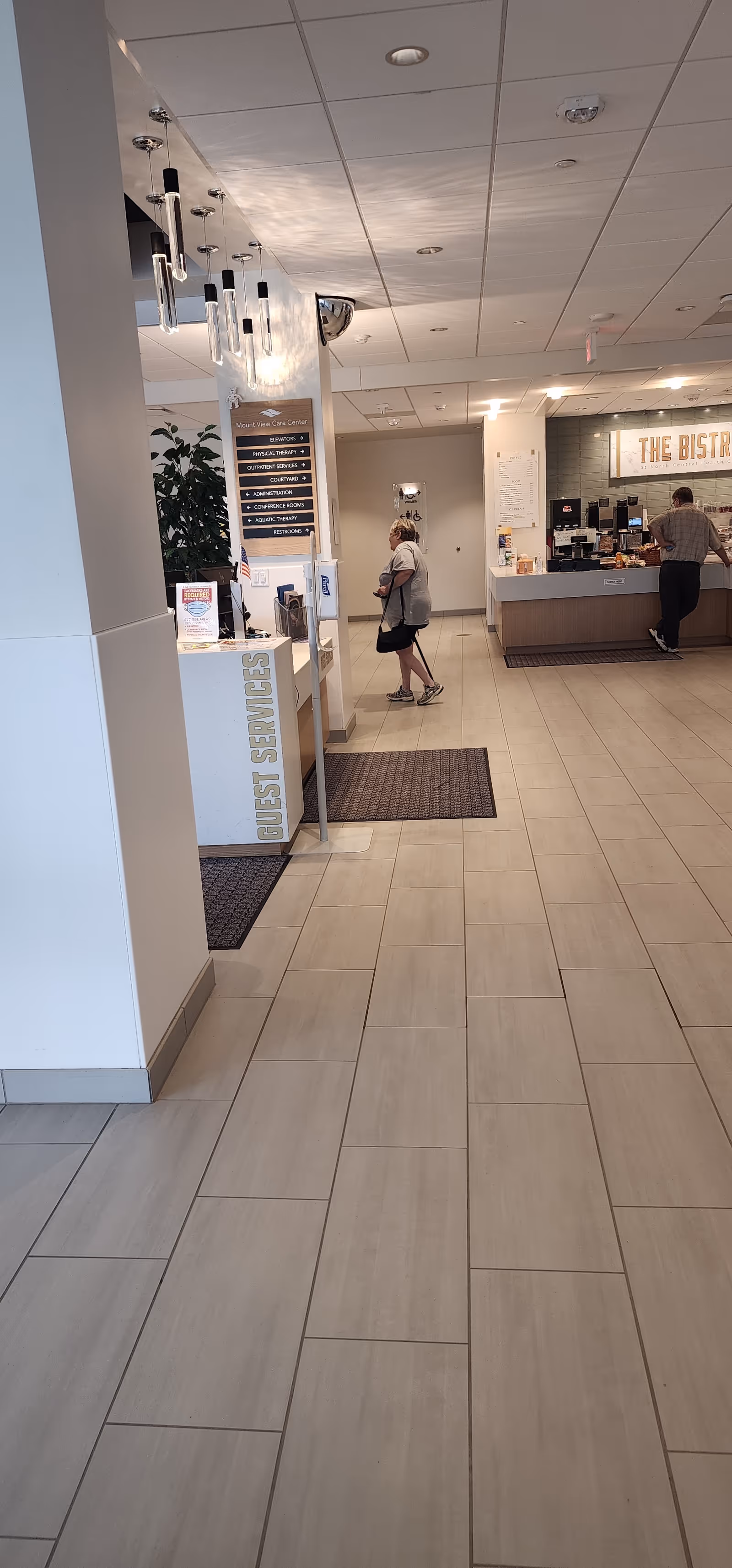 Lobby of a senior living facility with a front desk, plants, and a cafe.