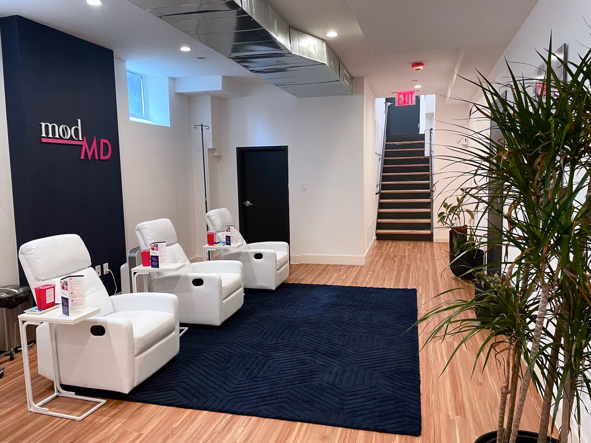 A modern facility lobby with white recliners, plants, and a dark accent wall featuring modMD.