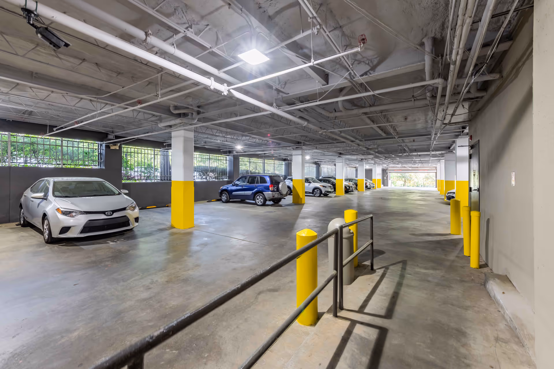 Indoor parking garage with parked cars, yellow safety bollards and painted support columns.