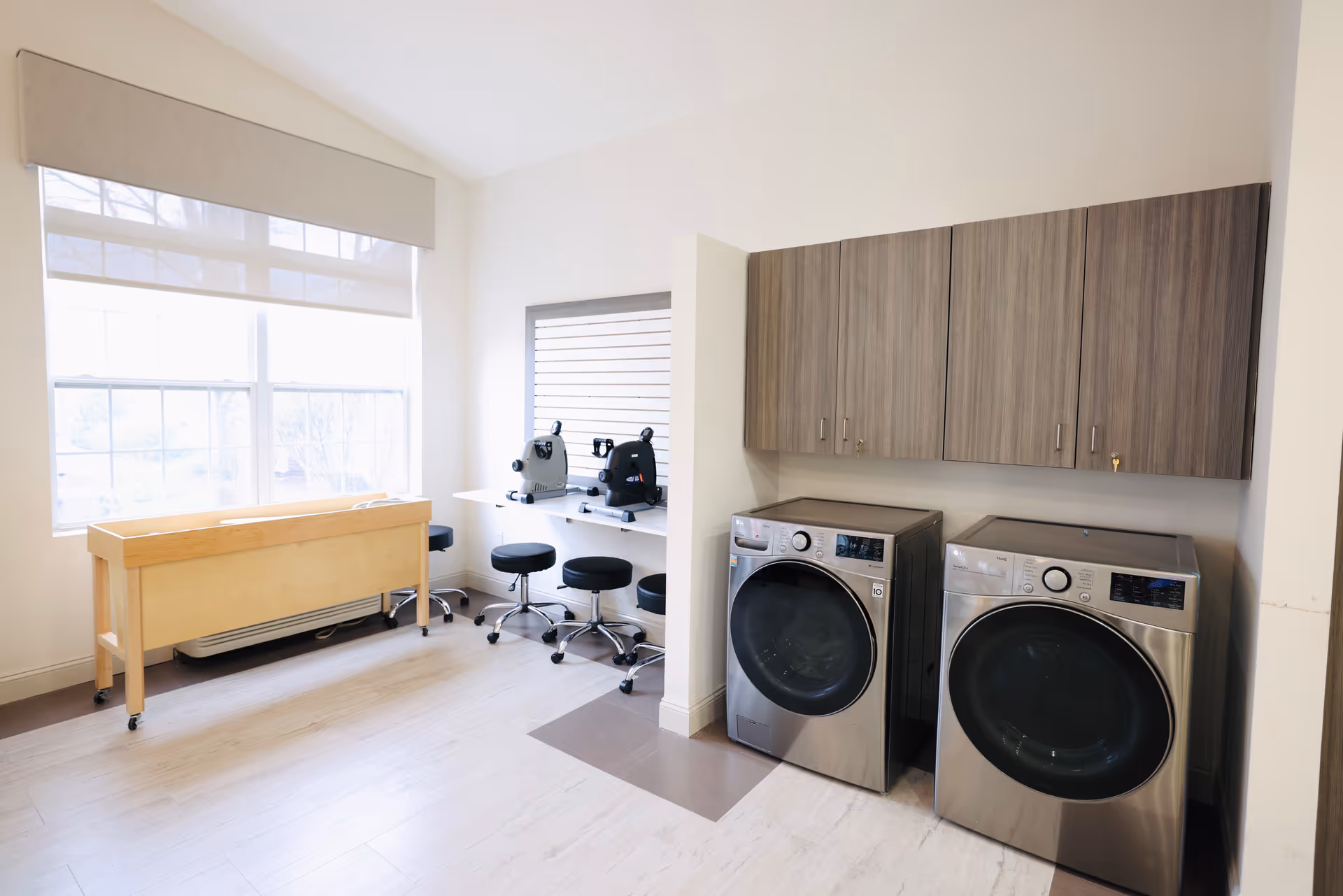 Laundry room with front load washers, cabinetry, counter, and seating area by a large window.