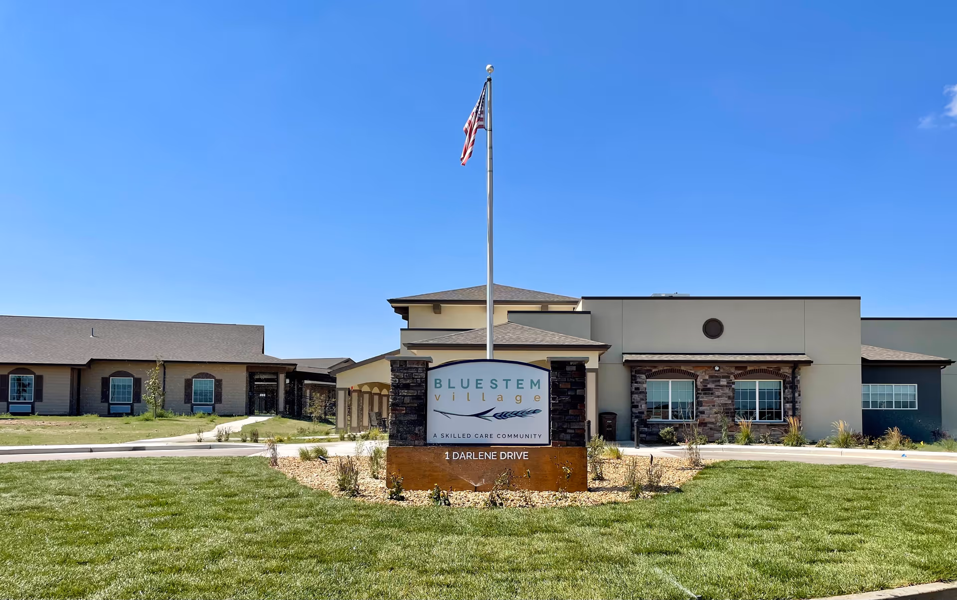 Front view of Bluestem Village senior living facility with flagpole and signage.