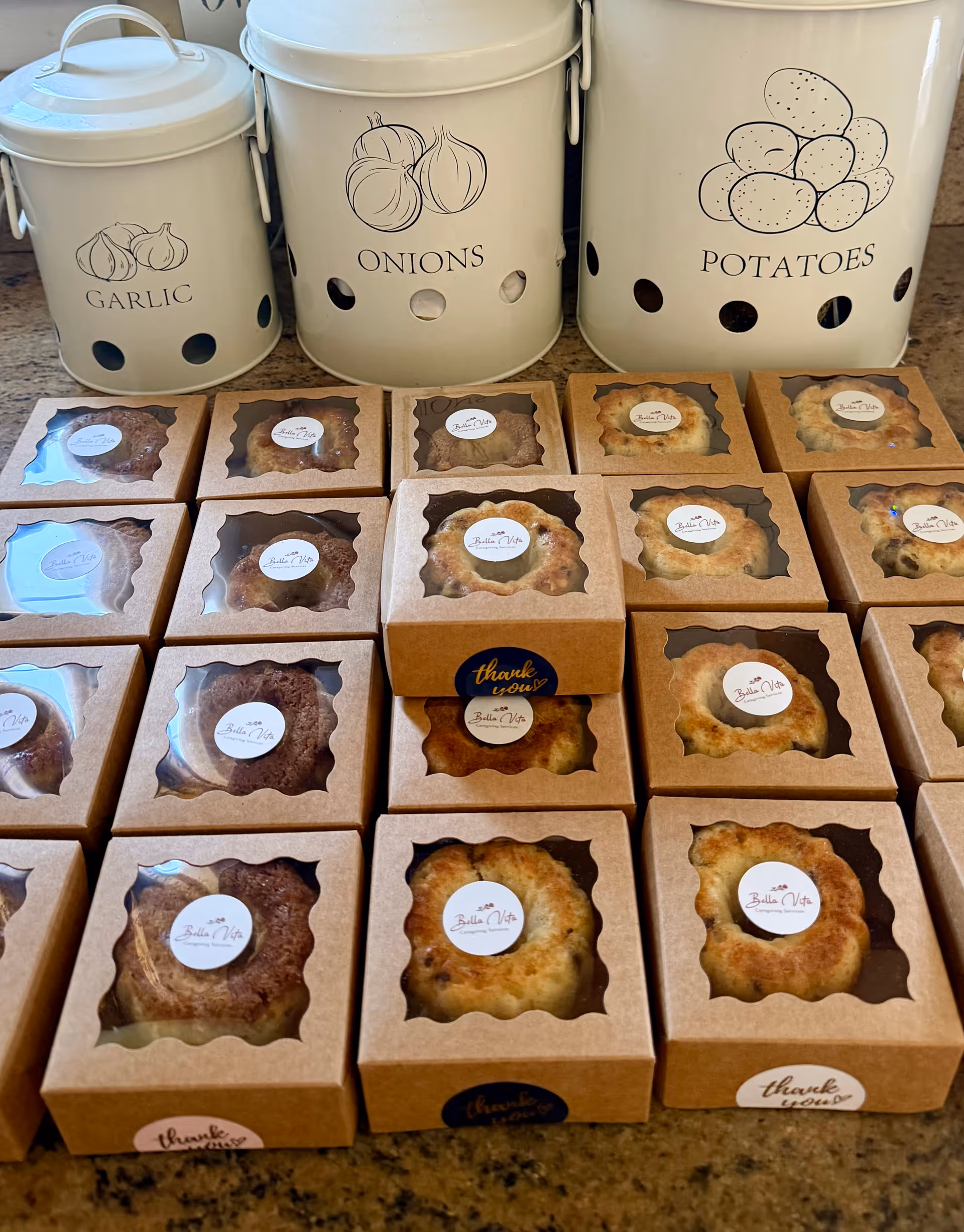 Row of pastry boxes on a kitchen counter with labeled garlic, onions, and potatoes canisters.