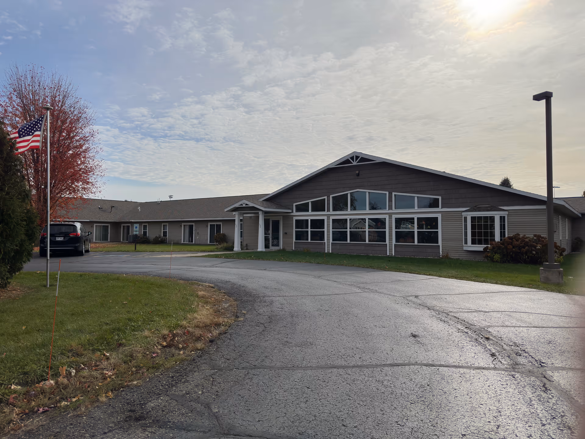 Exterior view of Prairie Ridge Assisted Living building with driveway, flagpole, and cars.