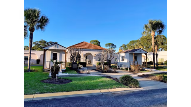 Exterior view of a senior care center with white cottages, palm trees, and a walkway.