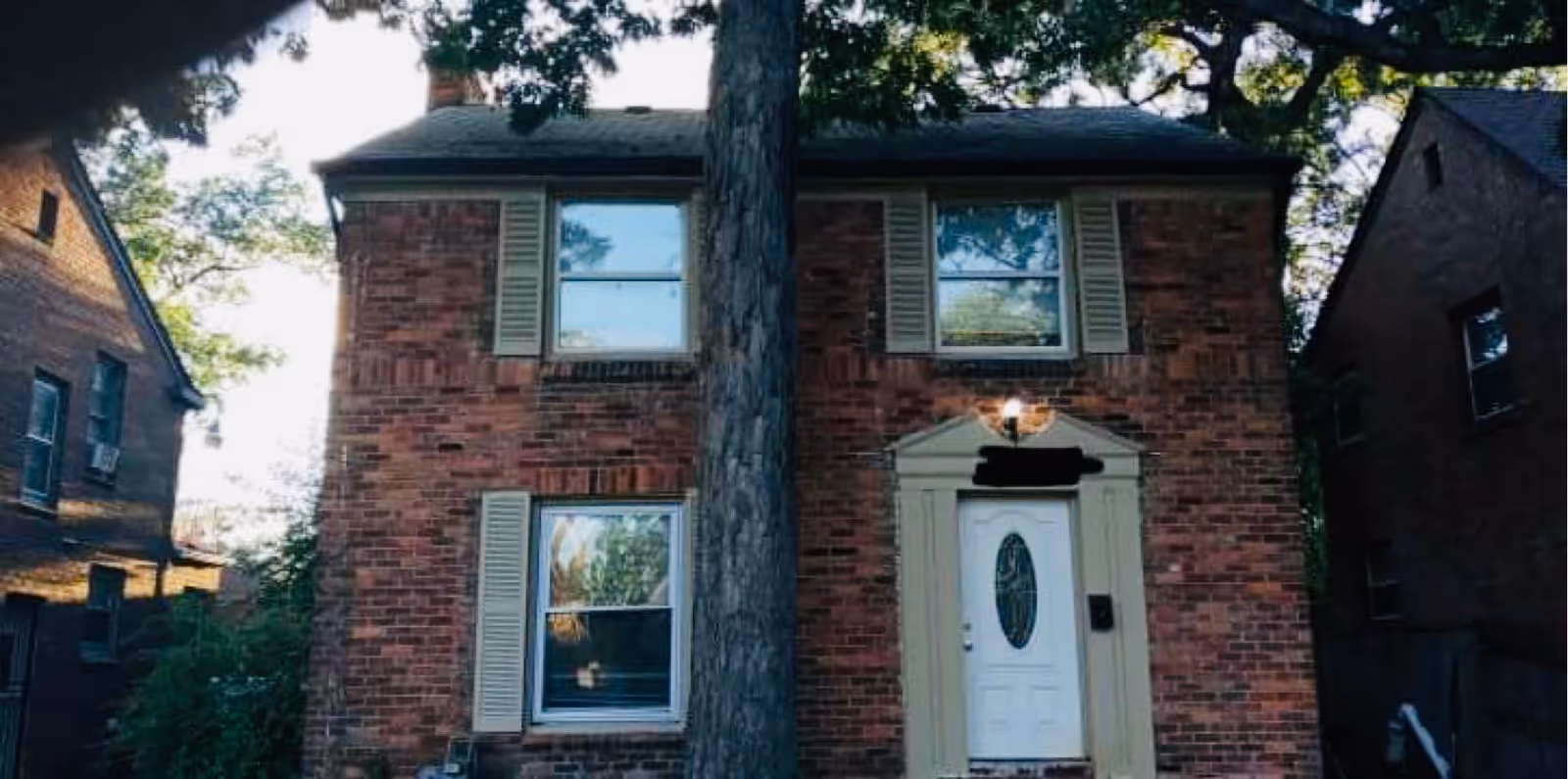 Brick two-story building with a white front door and a large tree in front.